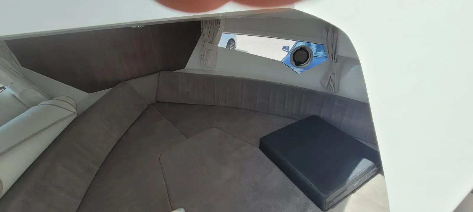 Interior of a modern boat featuring grey upholstered seating, a small black cushion, and an oval porthole window.